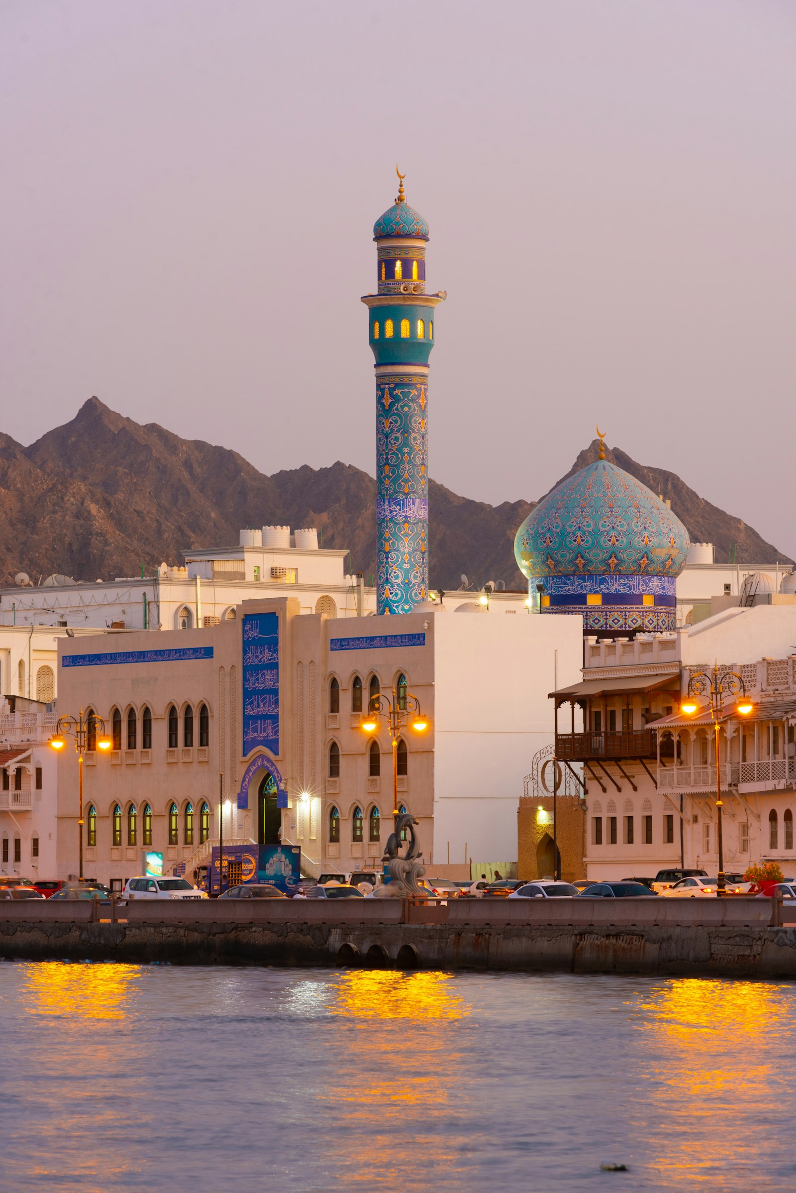 A mosque and waterfront buildings in Muttrah, Muscat, at dusk